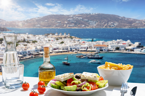 Tasty Greek food with salad, feta cheese and olive oil served with a view to the beautiful island of Mykonos, Greece, during summer time