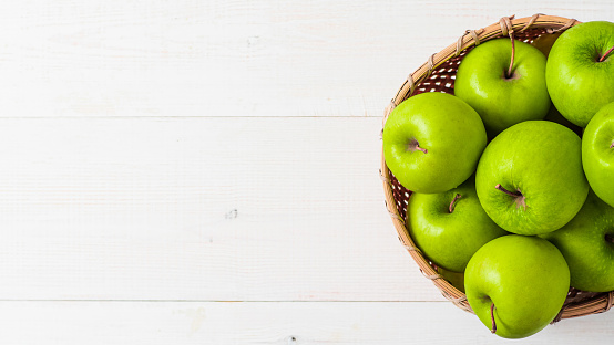 Apples harvest concept. Braided Bamboo Basket with green apples on white wooden background with copy space for text or design. Top down view or flat lay. Banner