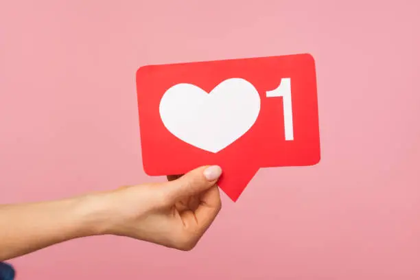 Photo of Closeup of hand holding social media heart like icon with number one, recommendation to support content