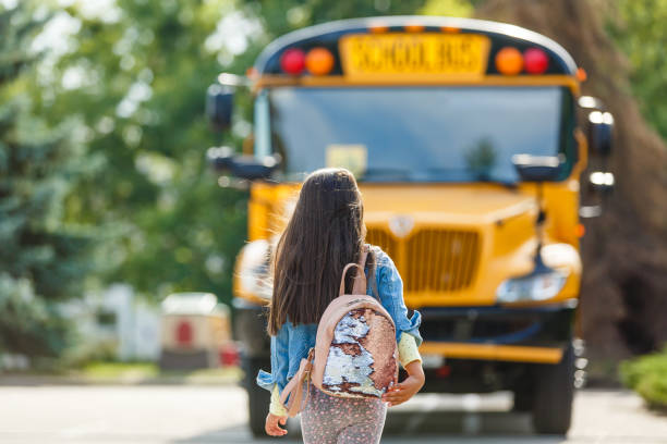 little girl standing by a big school bus door with her pink backpack. - blond hair carrying little girls small imagens e fotografias de stock