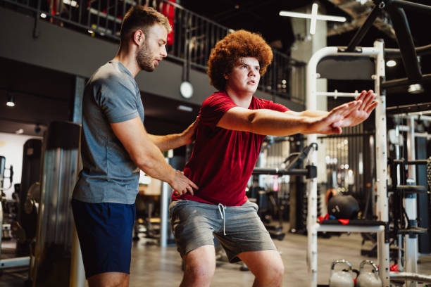 istock Overweight young man exercising gym with personal trainer 1220298493