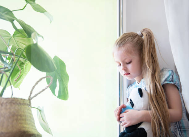 istock Sad child girl by the window 1220298657