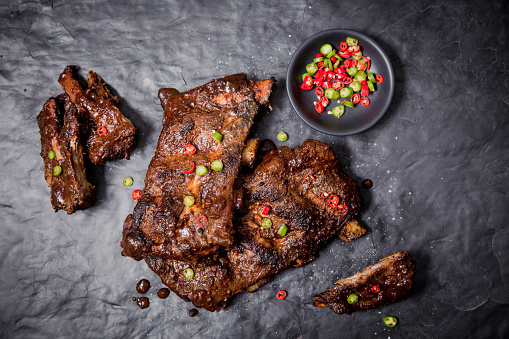 Beef Ribs served with red and green chilli's on black marble board.