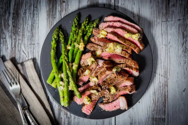Rump steak cut in strips served with asparagus on a round black plate and cutlery.