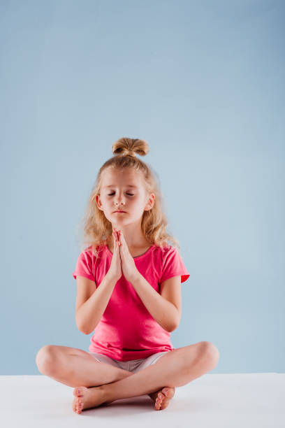 istock small girl meditating in yoga pose, isolated on blue 1220300948