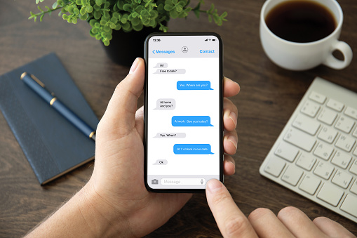 male hand holding phone with app messenger on the screen over table in the office