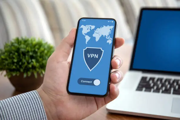Photo of male hand holding phone with app vpn over table laptop
