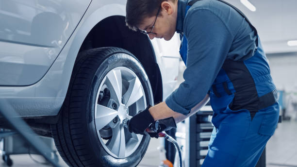 mechanik w niebieskim kombinezonie odkręca nakrętki lug za pomocą pneumatycznego klucza udarowego. repairman pracuje w nowoczesnej usługi czystego samochodu. specjaliści usuwają koło, aby naprawić element w pojeździe. - lug nuts zdjęcia i obrazy z banku zdjęć