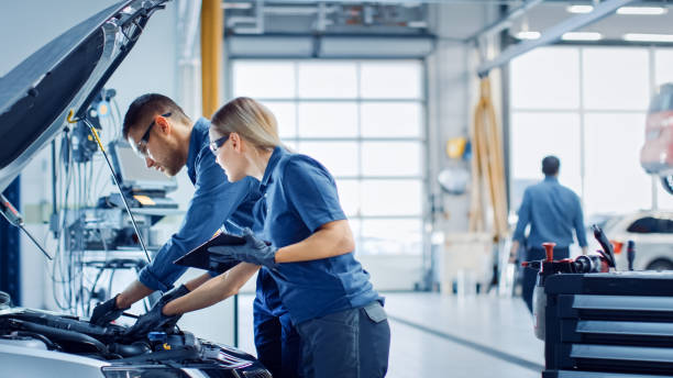 Two Mechanics in a Service are Inspecting a Car After They Got the Diagnostics Results. Female Specialist is Comparing the Data on a Tablet Computer. Repairman is Using a Ratchet to Repair the Faults. dos mecánicos en un servicio están inspeccionando un coche después de que obtuvieron los resultados de diagnóstico. la especialista femenina está comparando los datos en una tableta. el reparador está usando un trinquete para reparar las fallas.