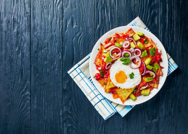 istock nachos with a fried egg, ham, crumbled panela cheese, avocado and tomato salsa on a white plate on a black wooden table, 1220308035