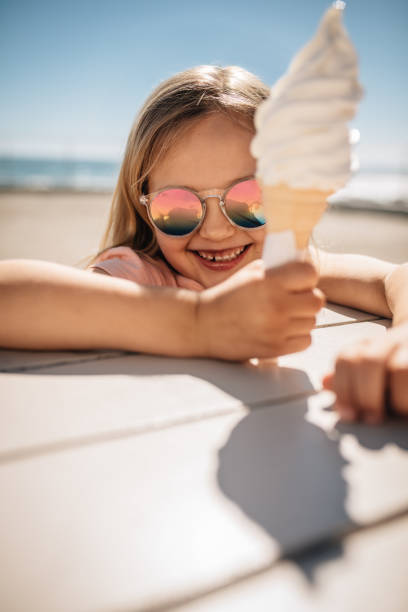 Beautiful girl holding a ice cream over a beach boardwalk. Young girl wearing sunglasses at the beach eating icecream on a summer day.