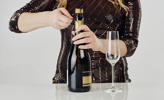Cropped shot of an unrecognizable woman using a cork screw to open a bottle of champagne in the studio
