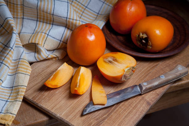 istock Whole ripe persimmon and sliced fruit on a wooden background. 1220315907