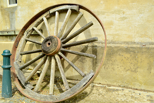 Old broken wooden wheel left next to a stone wall, rusty metal of the wheel details and sandy yellow colours of the wall.