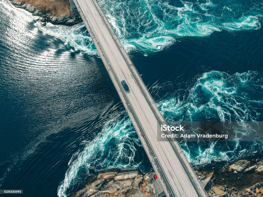 Car traversing bridge with water torrents beneath Torrents creating patterns in turquoise water underneath a bridge with a car traveling across it at Salstraumen near Bodo Norway Sustainable Resources Stock Photo