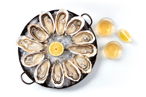 A dozen of oysters with wine and lemons, shot from the top on a white background, a flat lay