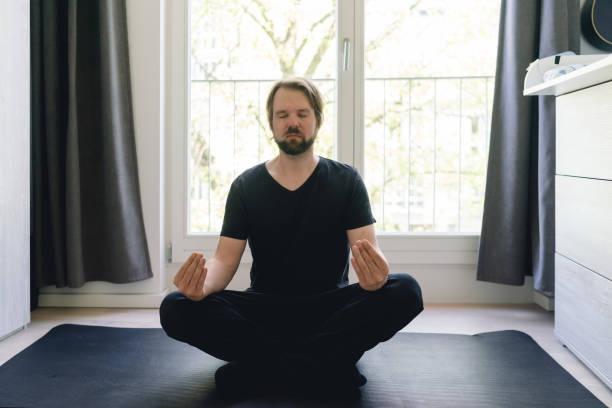 meditação de yoga em casa em uma posição de pernas cruzadas - men yoga meditating cross legged - fotografias e filmes do acervo