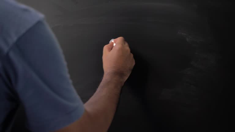 Close up male hand drawing sad emotion icon with chalk on chalkboard.