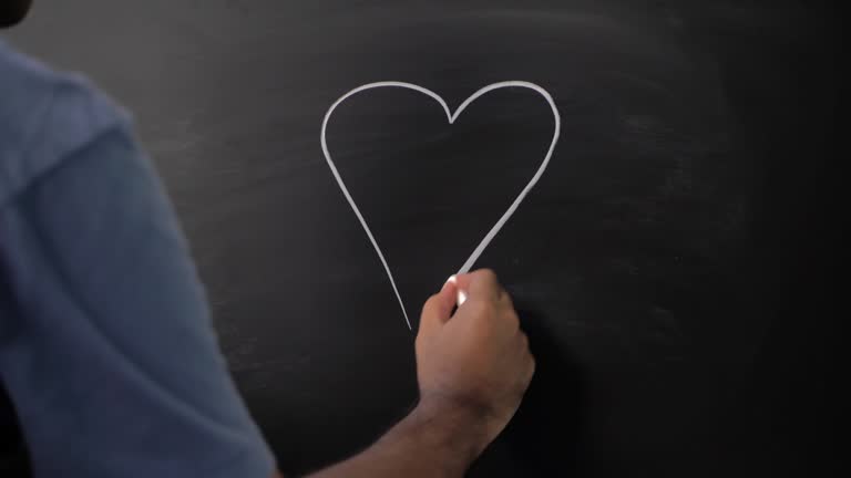 Close up male hand drawing heart icon with chalk on chalkboard.