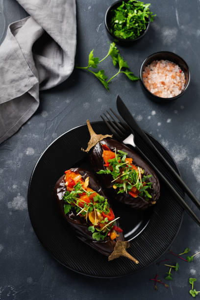 istock Baked stuffed eggplant with different vegetables, tomato, pepper, onion and parsley on a black stone or concrete table background. Top view. 1220328575