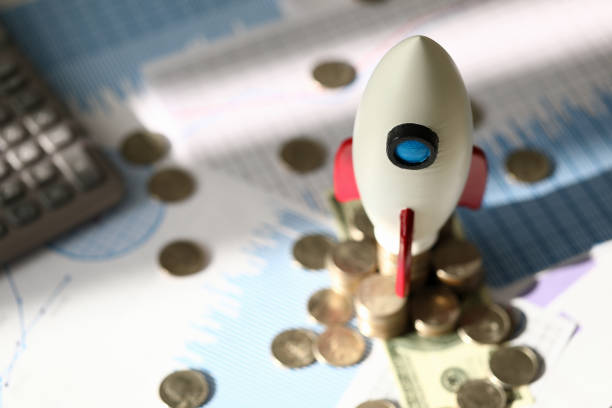 istock Toy space rocket stands on coins near calculator 1220328936