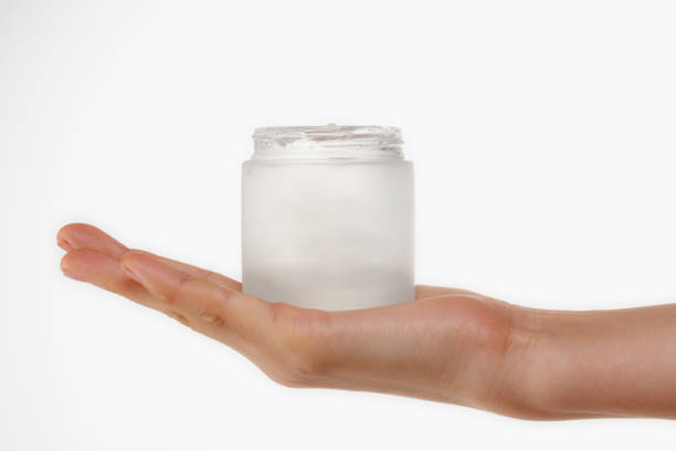 Attractive young woman applies facial cream from a jar. Isolated on white.