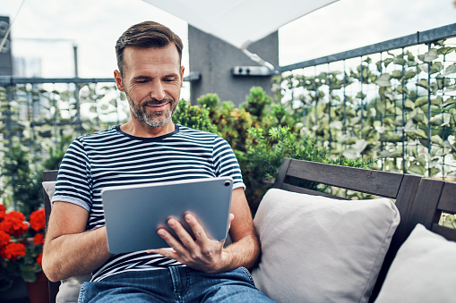 Cheerful man using tablet while sitting on house balcony