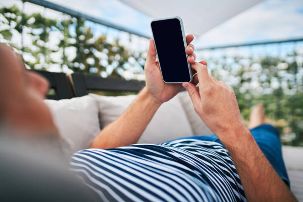 istock Close up of man using phone while lounging on apartment terrace 1220334805