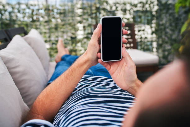 istock Close up of man looking at smartphone while lounging on patio sofa 1220335448