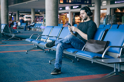 young cool man listening to music at the airport with headphones