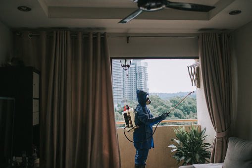 One woman in protective suit spraying and disinfecting the balcony exterminator pest control virus