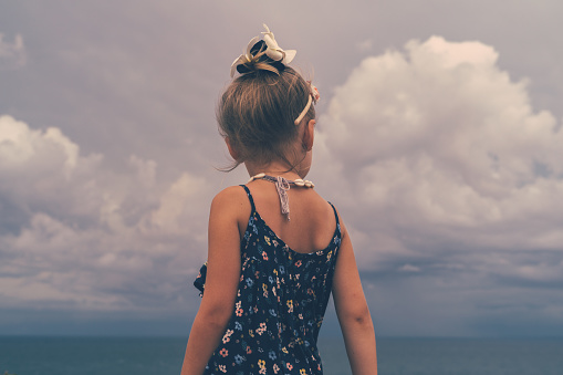little girl dressed in a blue dress  looking at the cloudy sky.