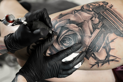 Close up image of the bearded tattoo male artist makes a tattoo on a female leg