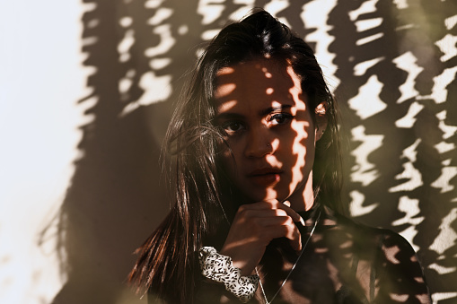 Cropped portrait of an attractive young woman posing alone against a wall with a shadow cast on her face