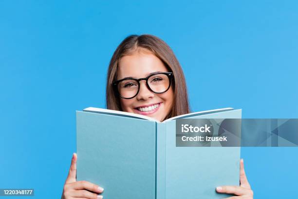 Pretty Teenage Girl Holding Book In Front Of Face Stock Photo - Download Image Now - Book, Eyeglasses, Back to School