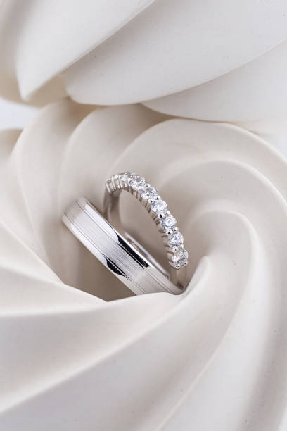 Pair of silver wedding rings with diamonds and matte surface on white textured background.