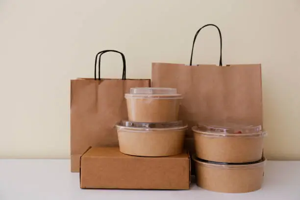 Photo of Stacks of ordered food and croceries in paper takeout containers and bags on table.