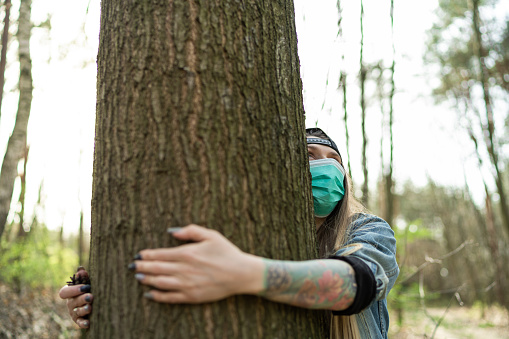 Casual Woman Hugging Tree in Park Wearing Face Protection Mask Against Coronavirus.