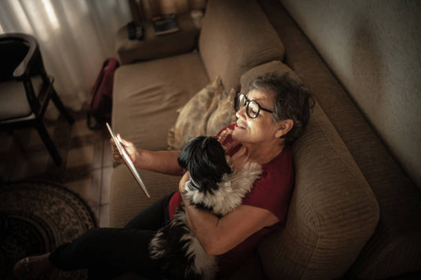 Senior woman doing a video call using a digital tablet at home Senior woman doing a video call using a digital tablet at home dog disruptagingcollection stock pictures, royalty-free photos & images