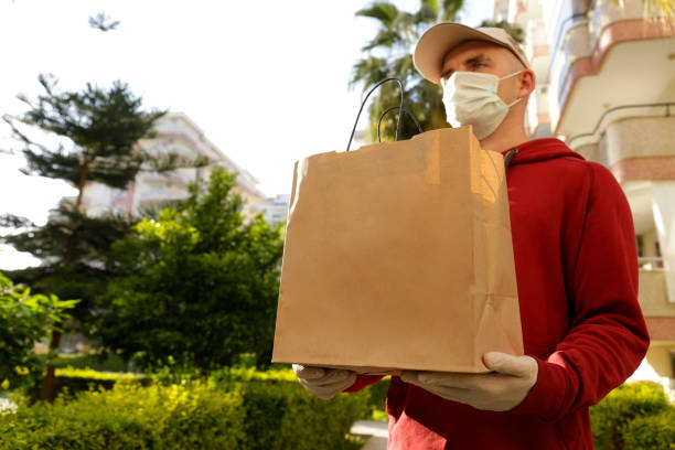istock Safe delivery service concept. Young courier wearing protective mask holding package. 1220349122