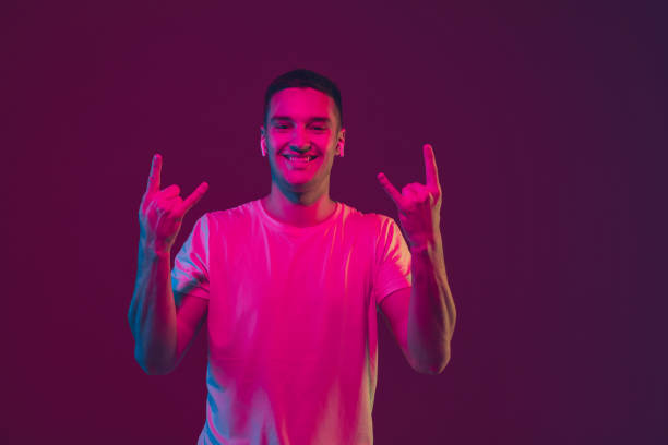 istock Caucasian man's portrait isolated on pink-purple studio background in neon light, using wireless earphones 1220352700