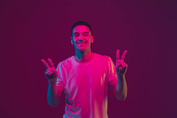 istock Caucasian man's portrait isolated on pink-purple studio background in neon light, using wireless earphones 1220352711