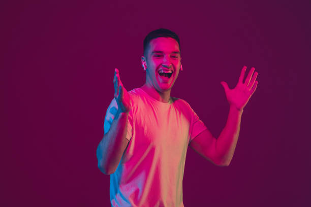 istock Caucasian man's portrait isolated on pink-purple studio background in neon light, using wireless earphones 1220352720