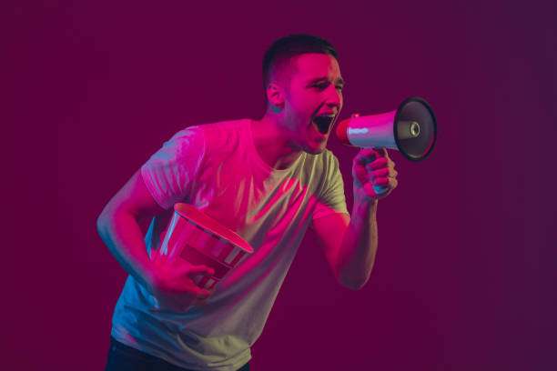 istock Caucasian man's portrait isolated on pink-purple studio background in neon light, using speaker 1220352746