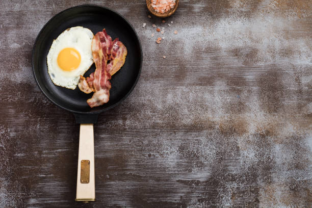 desayuno inglés tradicional con huevos fritos y tocino en sartén de hierro fundido sobre fondo de hormigón oscuro. vista superior. - photography metal traditional culture full fotografías e imágenes de stock