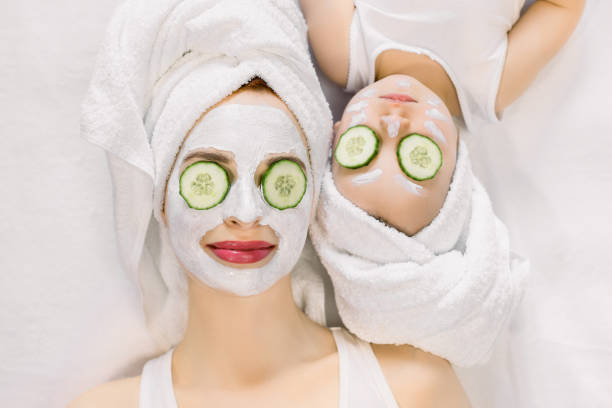 Mother and little daughter having spa procedures together. They are in white bath towels on head and with slices of cucumber on their eyes. Woman has white facial mask on her skin Mother and little daughter having spa procedures together. They are in white bath towels on head and with slices of cucumber on their eyes. Woman has white facial mask on her skin. women facial mask mud cucumber stock pictures, royalty-free photos & images