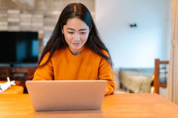 молодая стильная женщина с помощью ноутбука в домашних условиях - japanese ethnicity college student student asian ethnicity стоковые фото и изображения