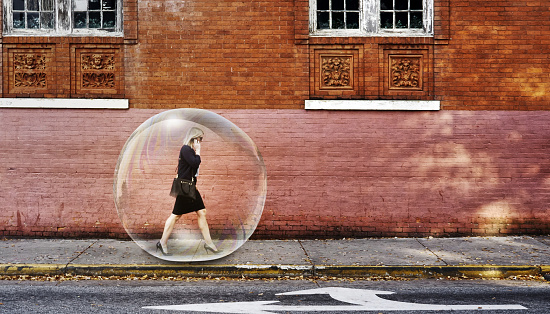 Businesswoman in a bubble for protection walking on a sidewalk using mobile phone in the city.