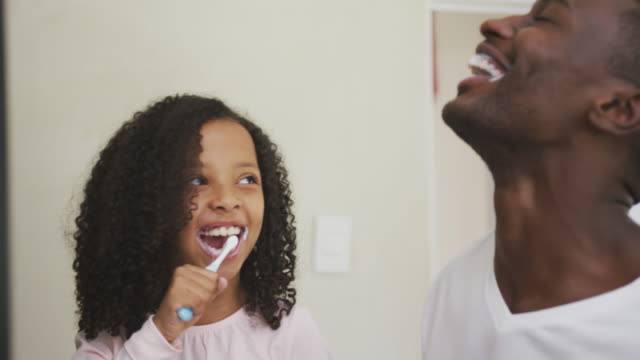 African american father and daughter brushing their teeth