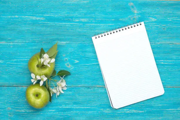 two green apples and open blank notepad on turquoise wooden background
